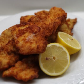 Shows a plate with pieces of schnitzel and a lemon sliced in half