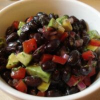 Shows a white bowl that contains Black Bean and Avocado Salad
