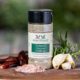 Shows a spice bottle with the My Sage Gourmet label for Summer Garden Grilling sitting on a wood cutting board and surrounded by an assortment of herbs, salt, chilis, and various spices