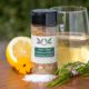 Spice bottle with My Sage Gourmet label for Lemon Thyme Chardonnay Infused Seasoning and Rub set on a cutting board with half an orange, salt, fresh herbs, and a glass of chardonnay wine