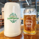 Shows a white German beer mug that says Frühlingsfest and a glass beer mug with beer in it that says Enegren Moorpark.