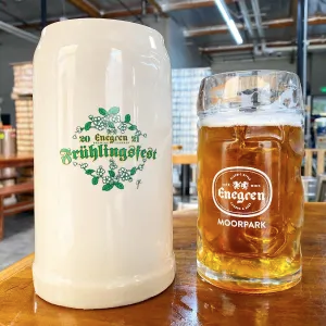 Shows a white German beer mug that says Frühlingsfest and a glass beer mug with beer in it that says Enegren Moorpark.